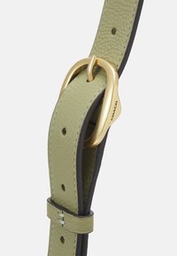 Zielono-oliwkowy skórzany pasek z okrągłą, złotą klamrą z wygrawerowanym napisem "Coach" oraz wieloma otworami do regulacji rozmiaru.