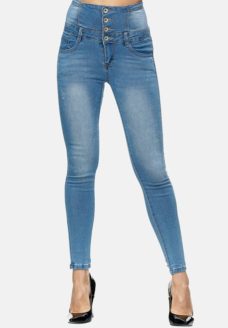 Jeans de tiro alto de color azul con una textura de mezclilla suave, cierre con cinco botones y dos bolsillos frontales, ajustándose en el tobillo. Combinados con tacones negros.