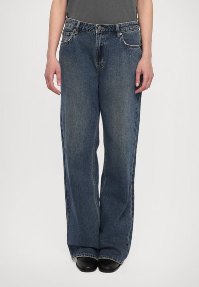 Kék farmer széles szárú jeans, elhalványult felülettel, ezüst színű kellékekkel, öt zsebbel és egyenes szabással, fekete cipővel viselve.