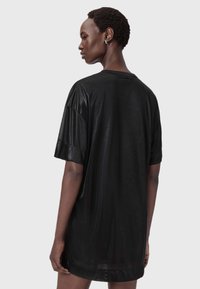Czarna, błyszcząca, oversize t-shirt z krótkim rękawem, luźny krój i asymetryczny dół. Miękka faktura z minimalistycznym wzornictwem.