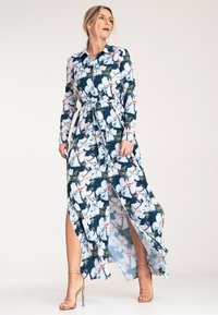 Kwiatowa sukienka maxi w granatowym kolorze z białymi i różowymi kwiatami, długie rękawy, zapinana na guziki, z talią podkreśloną i wysokimi rozcięciami po obu stronach.