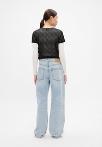 Top corto negro con textura de rayas horizontales sobre una camiseta de manga larga blanca, combinado con unos vaqueros de pierna ancha en azul claro que cuentan con bolsillos traseros.