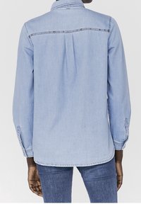 Light blue denim shirt with a buttoned back yoke, long sleeves, and a straight cut. Features a subtle texture and contrasting stitching accents.