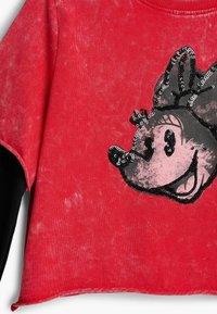 Punane puuvillasegune lühendatud dressipluus, millel on kulunud tekstuur ja esiküljel litridest Minnie Mouse'i kujundus.