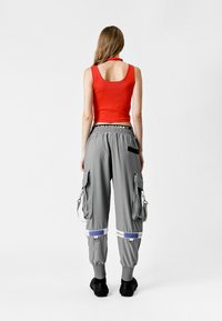 Top corto rojo combinado con pantalones cargo sueltos grises que cuentan con múltiples bolsillos laterales, cintura elástica y detalles en azul.