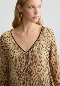 Maglione leggero lavorato a maglia con stampa leopardata nei toni del beige e marrone. Ha un collo a V e rifiniture nere lungo i bordi.
