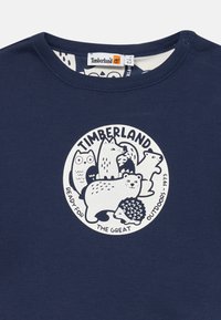 Mørkeblå bomulls T-skjorte med en sirkulær illustrasjon av forskjellige dyr, inkludert en bjørn, pinnsvin og ugle, med merkevarenavnet "Timberland."