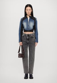 Cropped denim jacket with blue and black panels, silver zipper; gray high-waisted jeans; small burgundy handbag; black shoes.