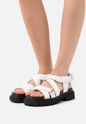 Witte sandalen met bandjes, gemaakt van geweven materiaal, met een dikke zwarte zool. Voorzien van een metallic gesp en een open teen ontwerp.
