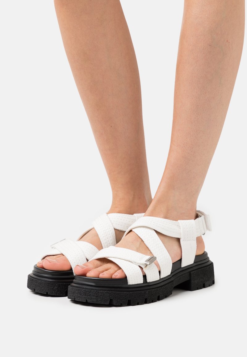 Witte sandalen met bandjes, gemaakt van geweven materiaal, met een dikke zwarte zool. Voorzien van een metallic gesp en een open teen ontwerp.