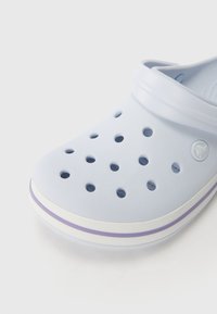 Light blue foam clog with ventilation holes, white sole, and a lavender stripe. Features a smooth texture and a circular logo on the side.