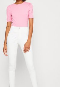 Top de mangas abullonadas rosa combinado con jeans ajustados blancos. El top tiene un escote redondo y una suave textura de algodón; los jeans cuentan con un cierre de botón.