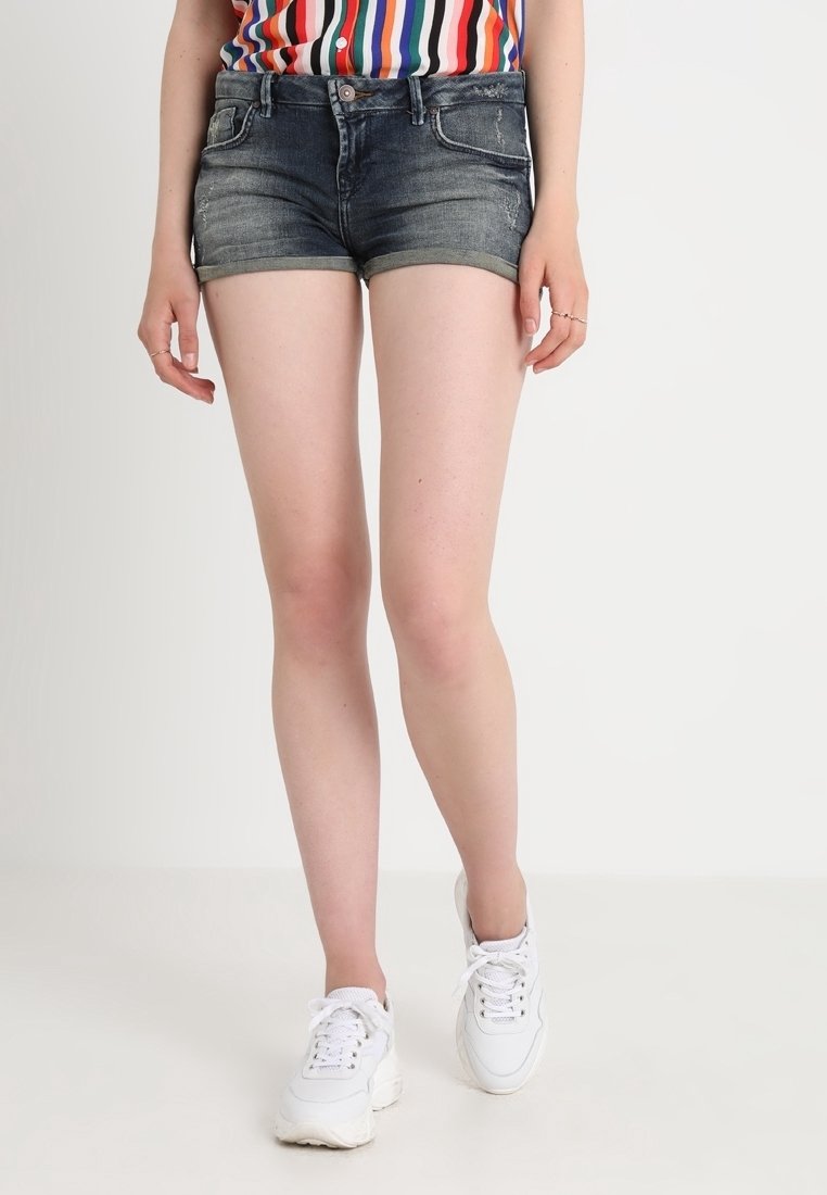 Krótkie spodenki dżinsowe w ciemnym odcieniu z lekkim wyblaknięciem, z pięcioma kieszeniami, postrzępionym dołem, zestawione z białymi trampkami.
