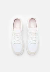 Baskets blanches avec une tige en mesh et des accents en daim, présentant un design à lacets, un col rembourré et un logo sur la languette.