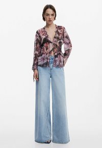 Lilledega blouse, millel on räpane kaelus, nupud ees ja laiad varrukad, koos lõdva helesinise teksapükstega.