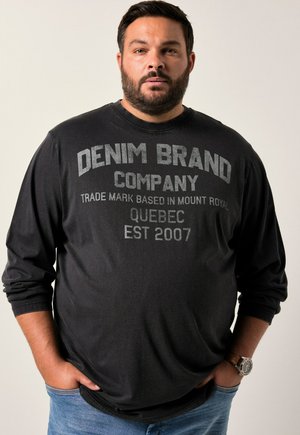 Schwarzes Langarm-T-Shirt mit "DENIM BRAND COMPANY" in Grau bedruckt. Baumwollmischung, lockere Passform, getragen mit blauen Jeans und einer Armbanduhr.
