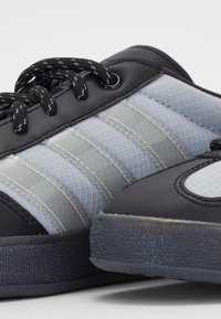 Black athletic shoes with gray mesh panels, textured rubber sole, and patterned laces. Features stitched accents and a rounded toe design.