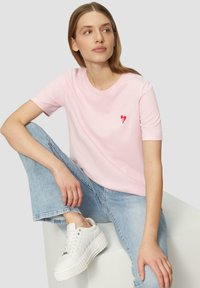Lichtroze katoenen t-shirt met een klein rood hartontwerp op de linkerkant van de borst. Gecombineerd met lichtblauwe jeans en witte platform sneakers.