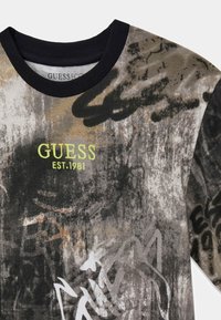 Bluza z nadrukiem z czarno-szarym abstrakcyjnym wzorem, prążkowany kołnierz, z logo "GUESS EST.1981" w kolorze limonkowej zieleni. Miękka w dotyku.