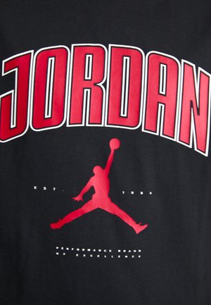 Musta t-paita, jossa on suuri punainen teksti "JORDAN", punainen siluetti koripallon pelaajasta ja lisävalkoista tekstiä "EST. 1984."