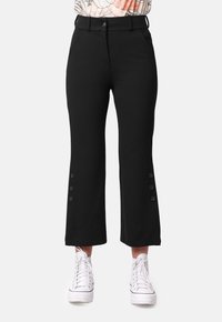 Pantalones cortos negros con cintura ajustada, bolsillos delanteros y botones en el dobladillo. Combinados con zapatillas blancas, exhibiendo un look casual.