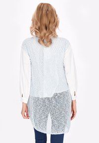 Cardigan lavorato a maglia azzurro chiaro con un intreccio aperto, caratterizzato da maniche lunghe, orlo arrotondato e una camicia interna bianca a contrasto visibile.