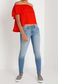 Röd off-shoulder topp med volangdetalj, ljusblå skinny jeans och svart-vita rutiga slip-on skor. Slät tyg och figurnära design.
