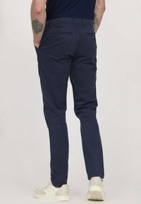 Pantalons en coton bleu marine avec une coupe slim, poches arrière ornées de boutons marron, associés à des baskets de couleur claire.