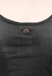 Κοντινό πλάνο στο ντεκολτέ μαύρου υφάσματος τζιν με μικρή οβάλ εγκοπή και ραμμένη λεπτομέρεια περιγράμματος.