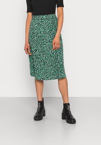 Falda midi floral verde con una cinturilla elástica, que presenta un patrón de acentos en blanco y negro. Combinada con botas negras de tacón grueso.