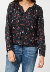 Svart blus med ett bladmönster i rött, lila och grönt. Har V-ringning och långa, rynkade ärmar. Slät tyg.