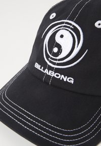 Căciulă din bumbac negru cu cusături albe, un emblemă circulară yin-yang și logo-ul "BILLABONG" brodat pe față.