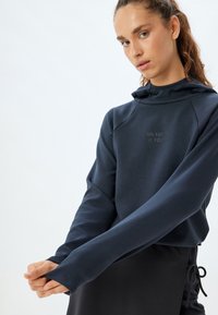 Sudadera azul marino con un cuello alto, que presenta el texto "EL FUTURO ES TUYO" en letras metálicas y mangas largas para mayor cobertura.