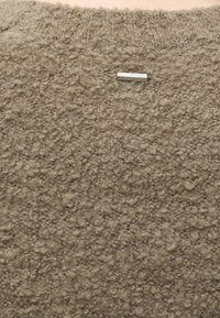 Ανοιχτό καφέ υφασμάτινη υφή από μαλλί με μια μικρή ορθογώνια μεταλλική πινακίδα κοντά στην πάνω άκρη.