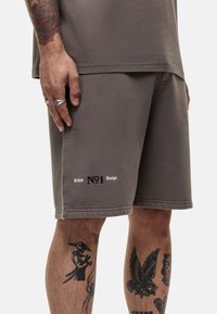 Pantaloni corti in cotone grigio con taglio dritto, con la scritta "British No1 Design" in nero. Texture liscia, design minimalista, senza tasche visibili.