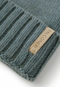 Stickad mössa i mjuk blågrön ull med ribbat mönster, med en tan läderetikett sydd på sidan.