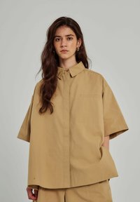Beige kortærmet skjorte med krave, enkelt brystlomme og en afslappet pasform. Lavet af letvægtsstof med en glat tekstur.