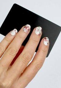 Weißer Nagellack mit floralen Mustern in Pink und schwarzen Ästen, präsentiert neben einer schwarzen Karte. Die Handhaut ist hell mit sichtbarer Textur.