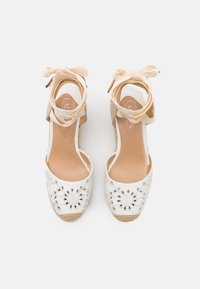 bílé espadrilky s květinovými výřezy na špičce, béžové kotníkové pásky s mašličkami a texturovanou tkanou jutu podešví.