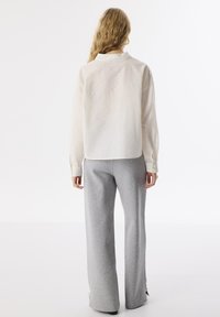 Chemise légère en crème avec col et poignets boutonnés, accompagnée d'un pantalon de survêtement gris à jambes larges, mettant en avant une texture douce et une coupe décontractée.