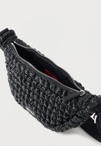 Μαύρη τσάντα χιαστί από δερμάτινο ρούστικ με ασημένιο φερμουάρ, μερικώς ανοιχτή που δείχνει το μαύρο εσωτερικό και ρυθμιζόμενο υφασμάτινο λουρί.