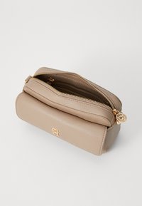 Pochette en cuir beige avec deux compartiments zippés, quincaillerie dorée et accent logo à l'avant. Texture douce et forme rectangulaire.