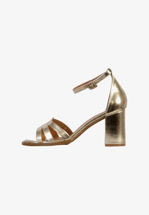 Gouden metallic hoge hak sandaal met een enkelbandje, open teen ontwerp en kruislings banddetail. Vierkante blokhak textuur.