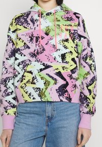 Felpa con cappuccio colorata in tonalità pastello con motivo a zigzag. Presenta lacci rosa e polsini, realizzata in morbido tessuto.