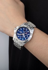 Orologio in acciaio inossidabile argentato con quadrante blu, funzionalità cronografo e lunetta marcata. Il bracciale ha una finitura spazzolata e un design a maglie.