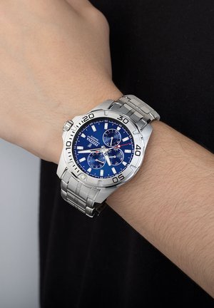 Montre en acier inoxydable argenté avec un cadran bleu, dotée de fonctionnalités chronographe et d'une lunette marquée. Le bracelet présente une finition brossée et un design à maillons.