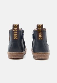 Botas de tobillo de cuero negro con acentos de tela marrón, suelas de goma texturizadas y correas traseras marrones con el nombre de la marca en relieve.