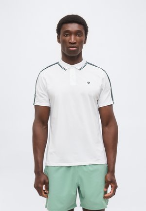 Άνδρας μοντέλο που φοράει λευκό πόλο με μαύρες ρίγες στα μανίκια και σορτς σε μέντα πράσινο χρώμα, στέκεται μπροστά σε έναν μονόχρωμο λευκό φόντο.