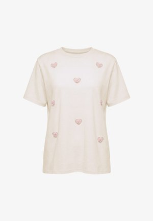 Beige kortærmet t-shirt med syv lyserøde hjerteformede applikationer jævnt fordelt på forsiden. Ingen synligt branding eller mønstre.