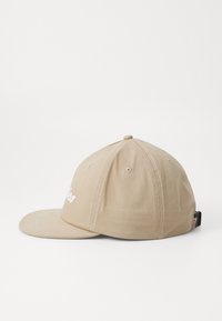 Beige színű baseball sapka pamutból, ívelt karimával, varrott részletekkel és hímzett felirattal az elején. Hátul állítható pánt.